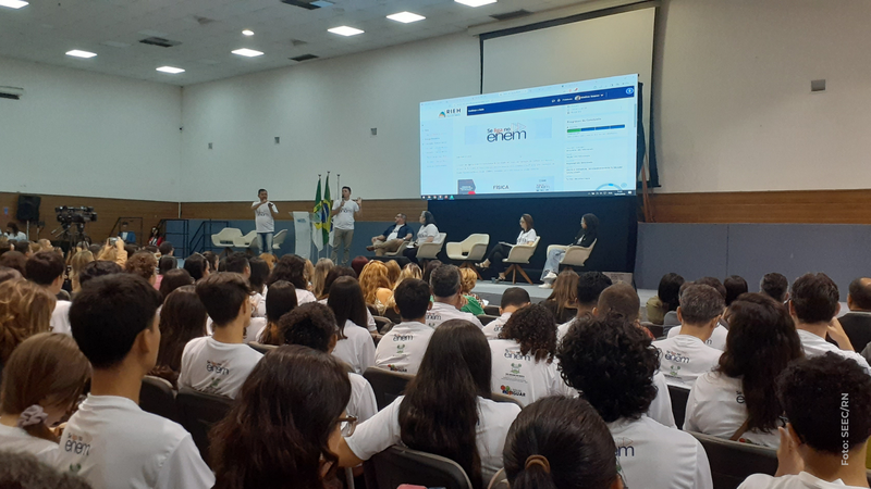 Geral do auditório lotado com estudantes no lançamento do "Se Liga no Enem", com palco e telão ao fundo.